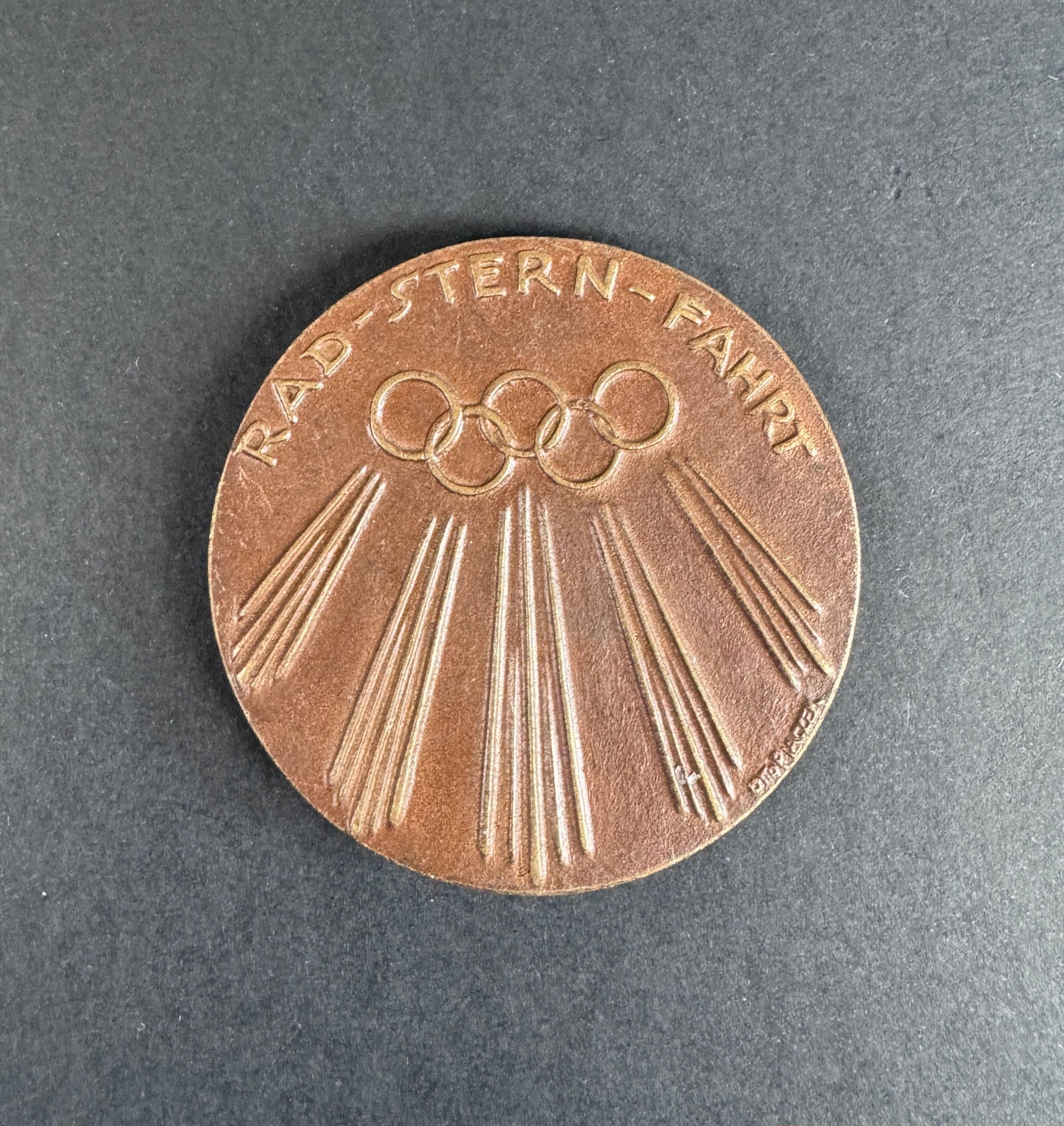 Bronze medal with Olympic rings on a dark gray background. For 9th Olympiad Berlin 1936.
