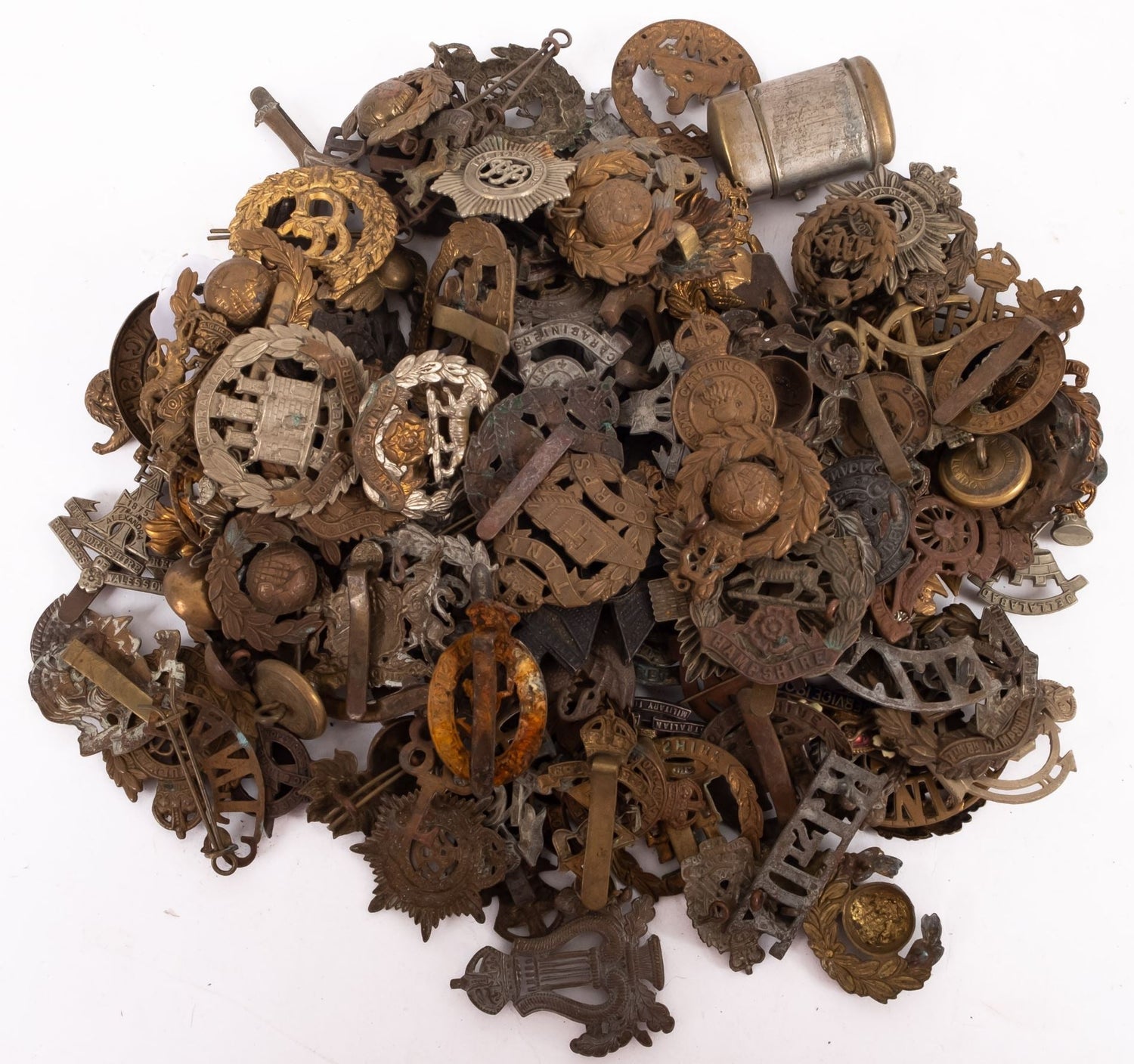 A large assortment of original British Army cap badges from various regiments, branches, and eras, piled together showing diverse metals, designs, and condition.