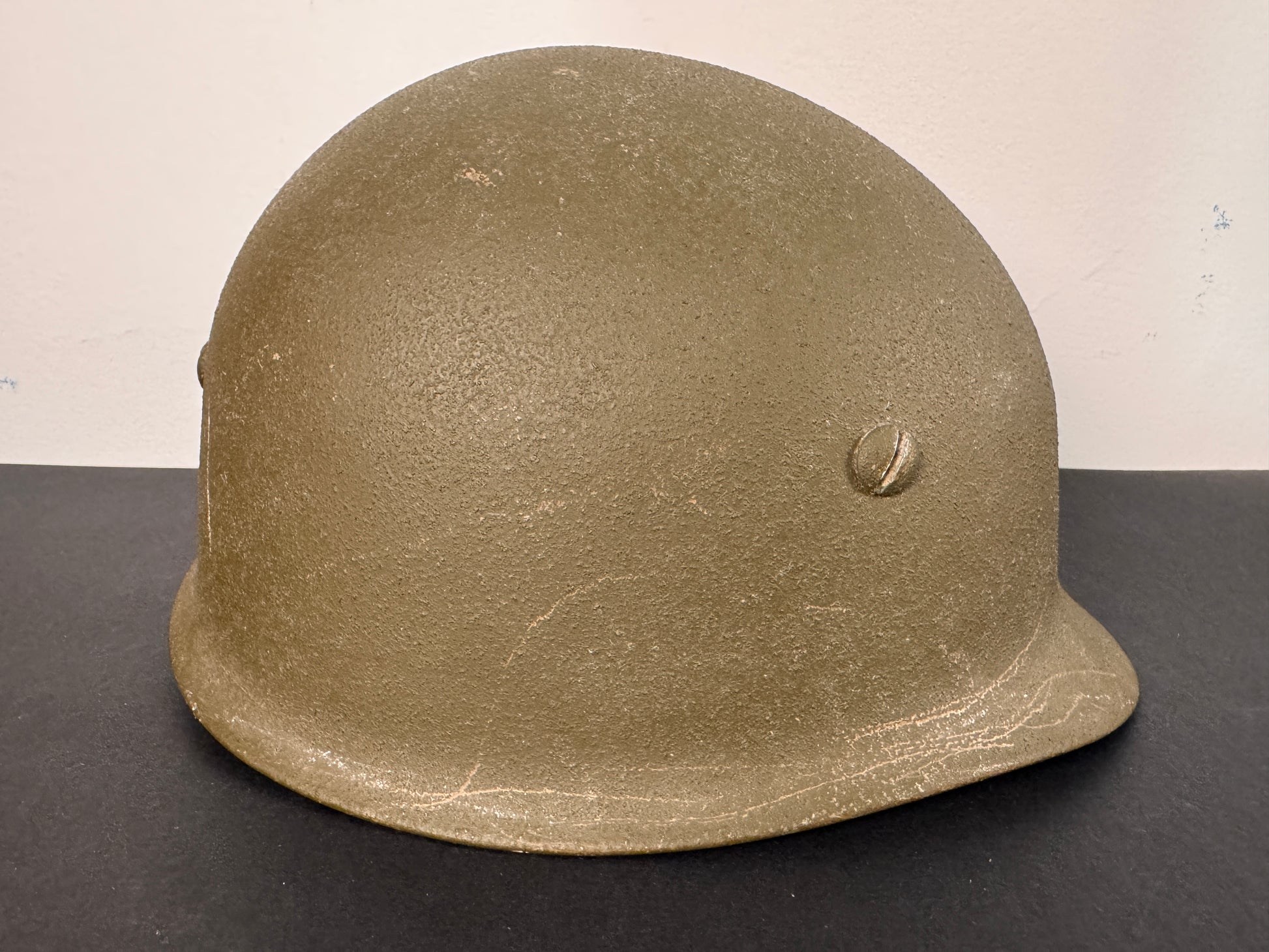 Green military helmet on a black surface with a white background