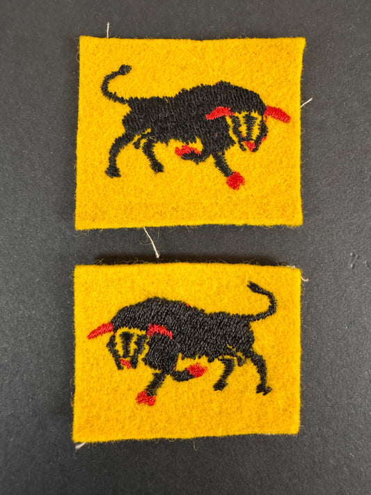 Two formation sign fabric patches of the 11th armoured division with rampant bull designs on a dark gray background