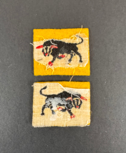 Two formation sign fabric patches of the 11th armoured division with rampant bull designs on a dark gray background