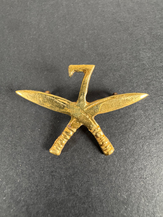 Gold-colored badge of the 7th gurkha rifle regiment, with crossed kukri swords on a dark gray background