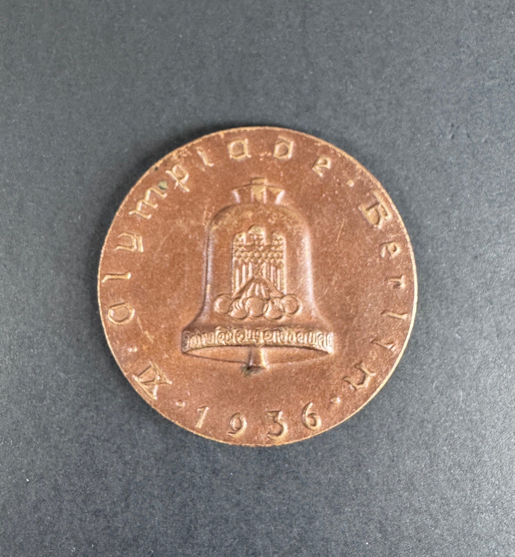 Bronze table medal with embossed design on a gray background. For 9th Olympiad Berlin 1936.