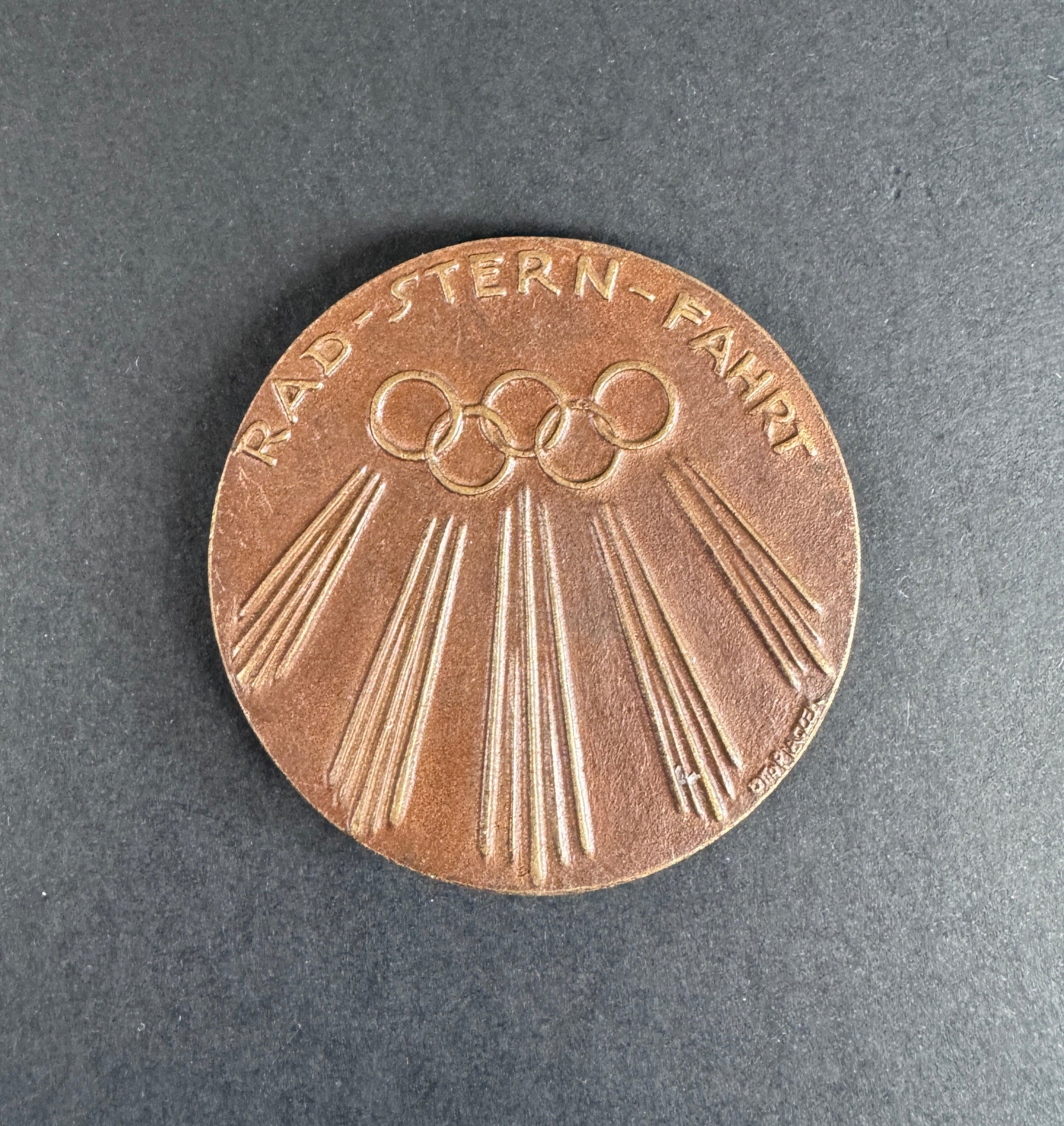 Bronze medal with Olympic rings on a dark gray background. For 9th Olympiad Berlin 1936.