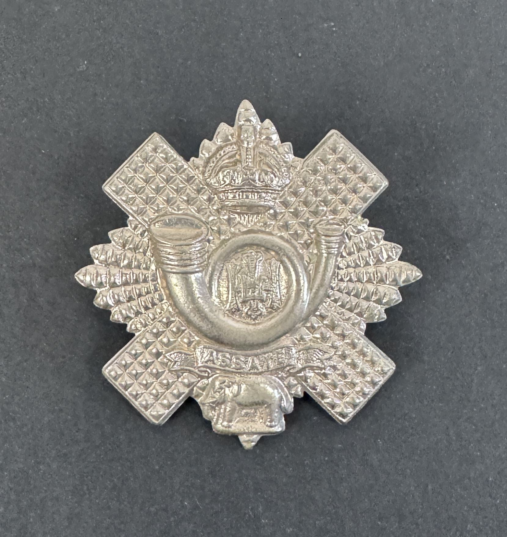 Silver military cap badge on a dark gray background