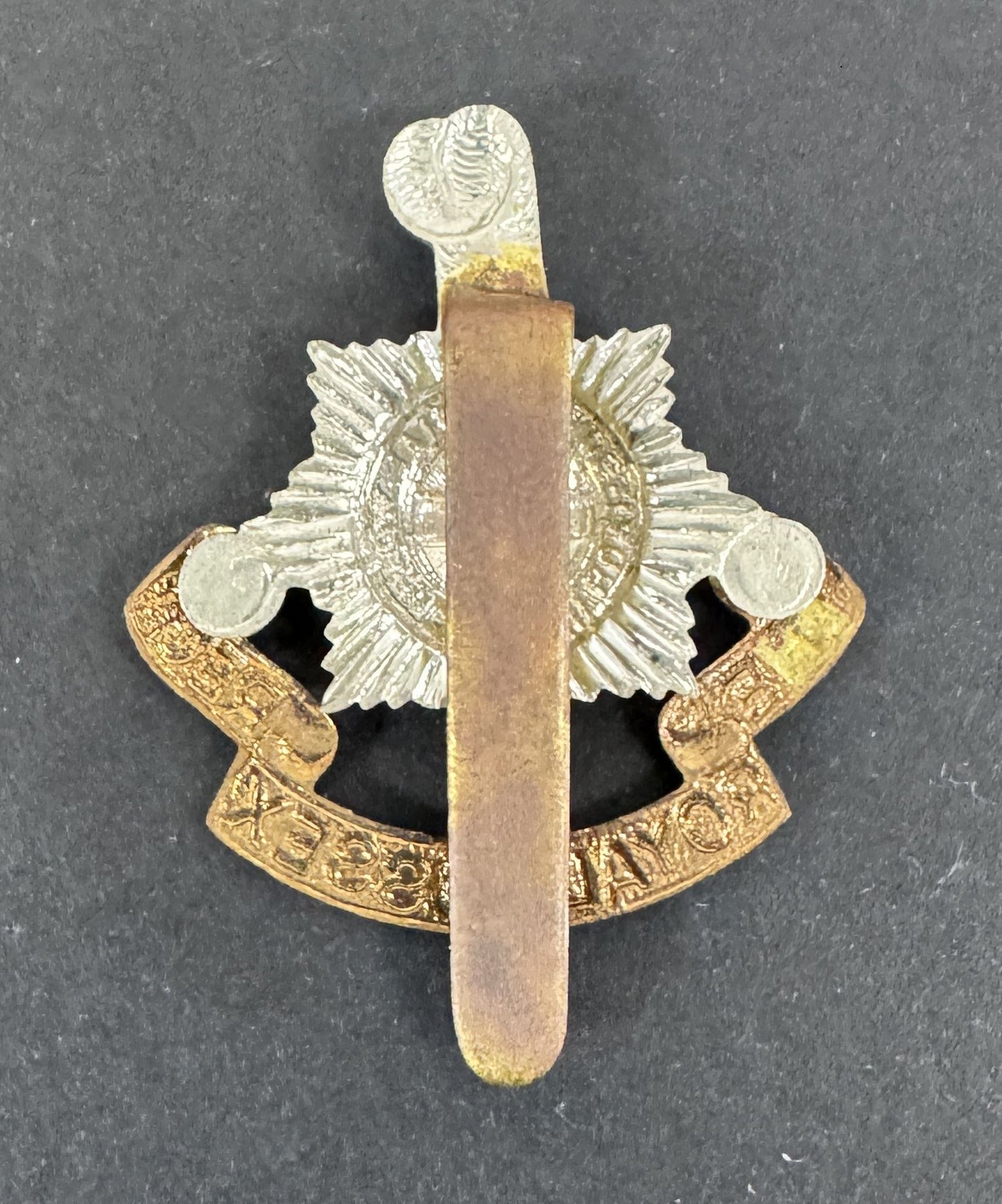 Decorative metal badge with a central emblem and a long, thin blade-like feature on a dark background