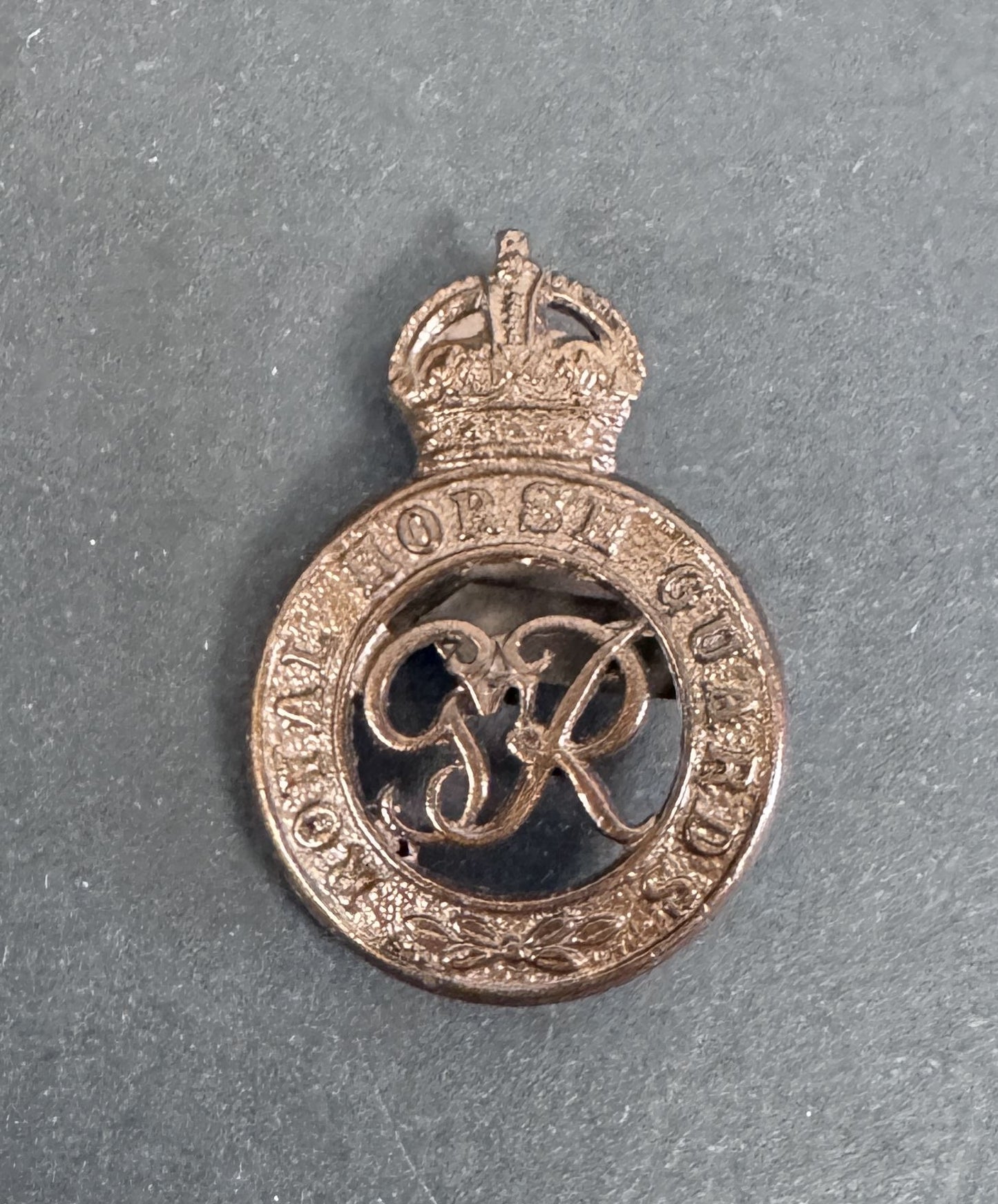 Bronze military badge with crown and letter 'R' on a gray background