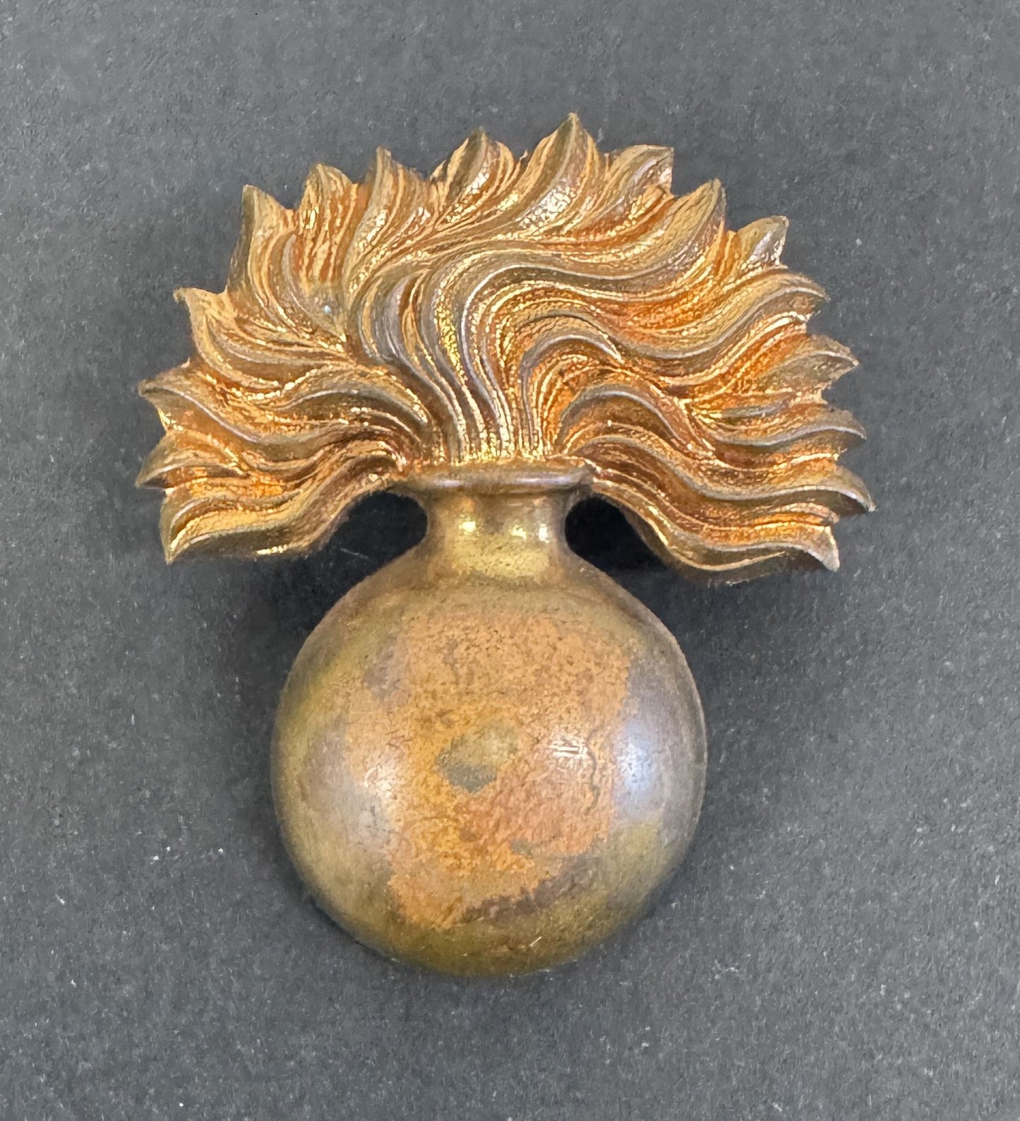 Decorative gold brooch with a spherical base and feather-like top on a dark background
