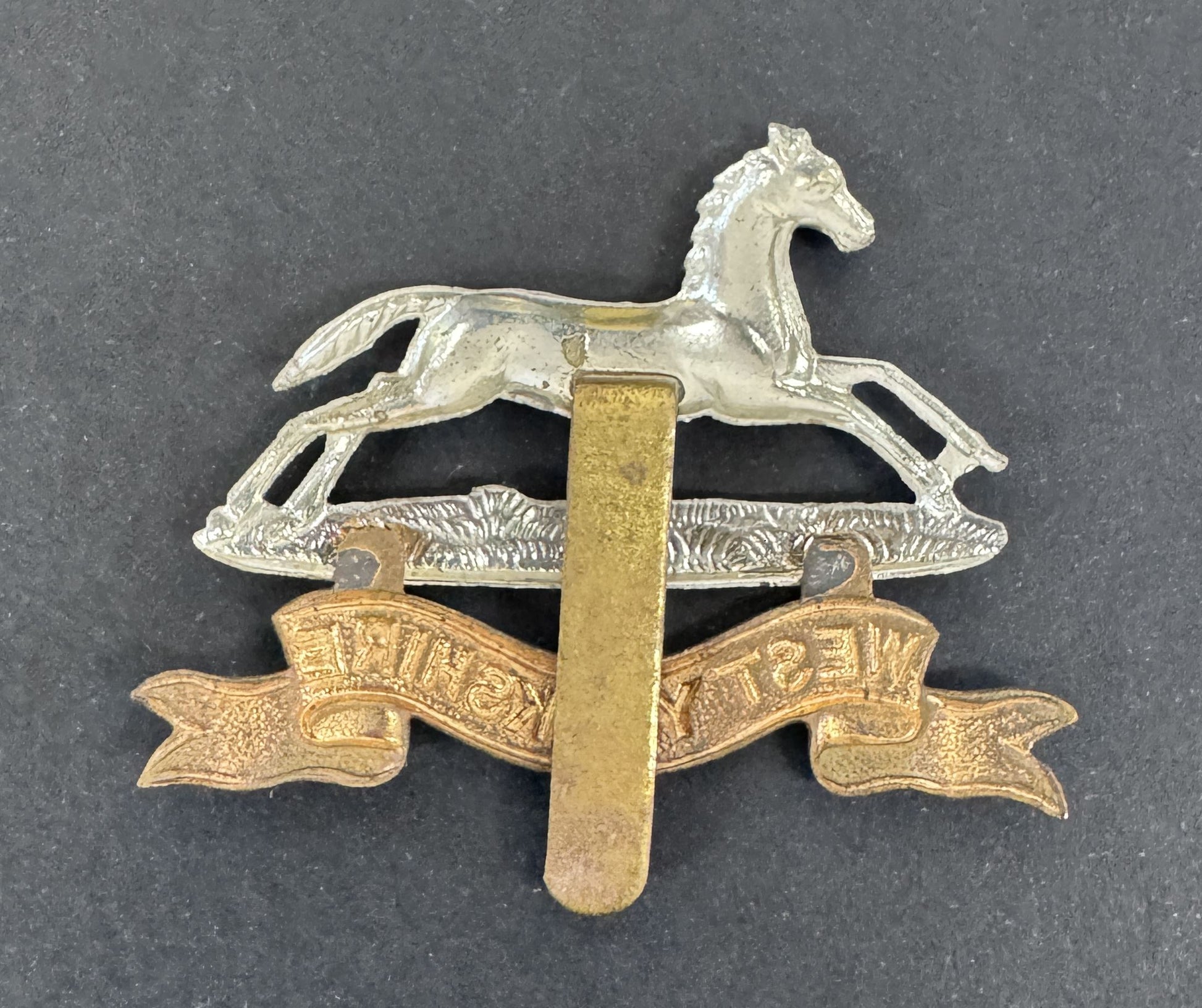 Metallic badge with a horse and banner design on a gray background