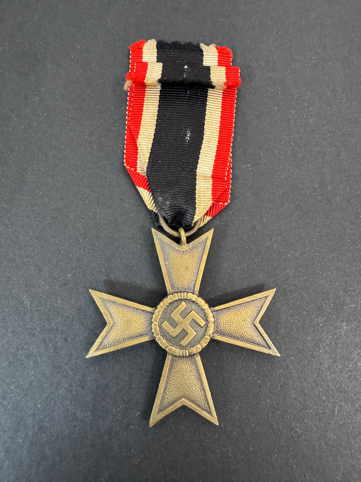 Nazi era cross medal with swastika emblem and ribbon on a gray background