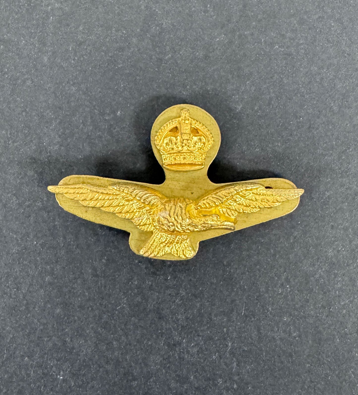Gold military badge with eagle design and crown emblem on a gray background