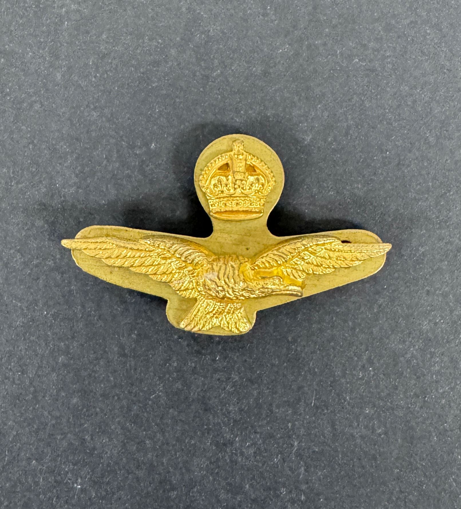 Gold military badge with eagle design and crown emblem on a gray background