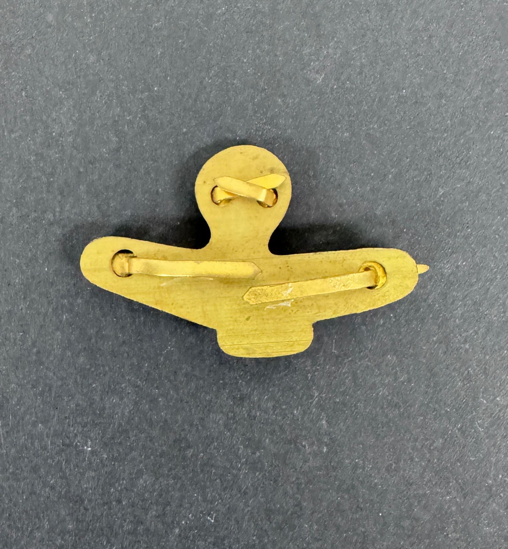 Gold-colored metal clip on a gray background, reverse of RAF officer's badge