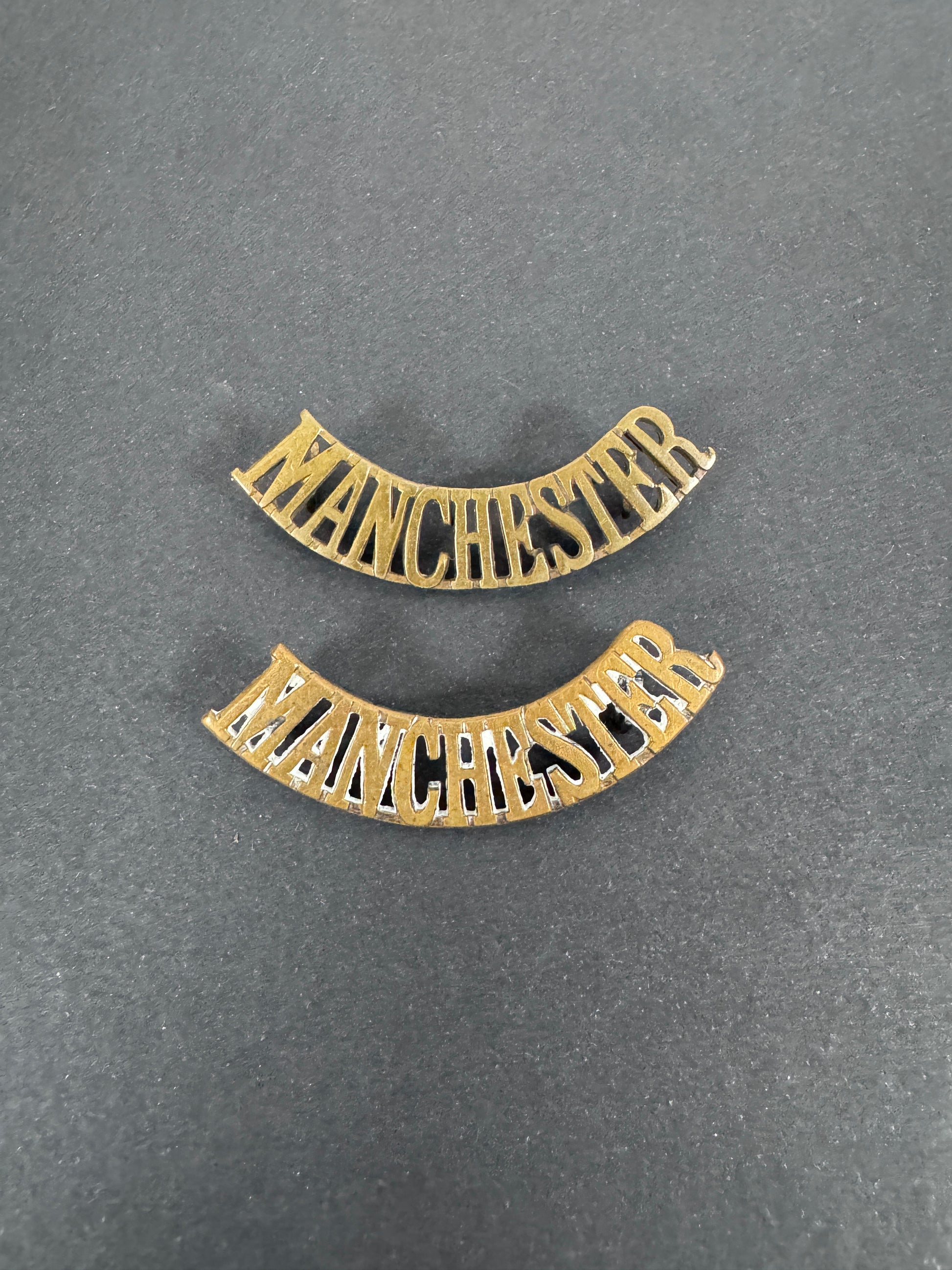 British Army Manchester Regiment Shoulder Title Badges (Pair) – A matching pair of original uniform shoulder titles of the...