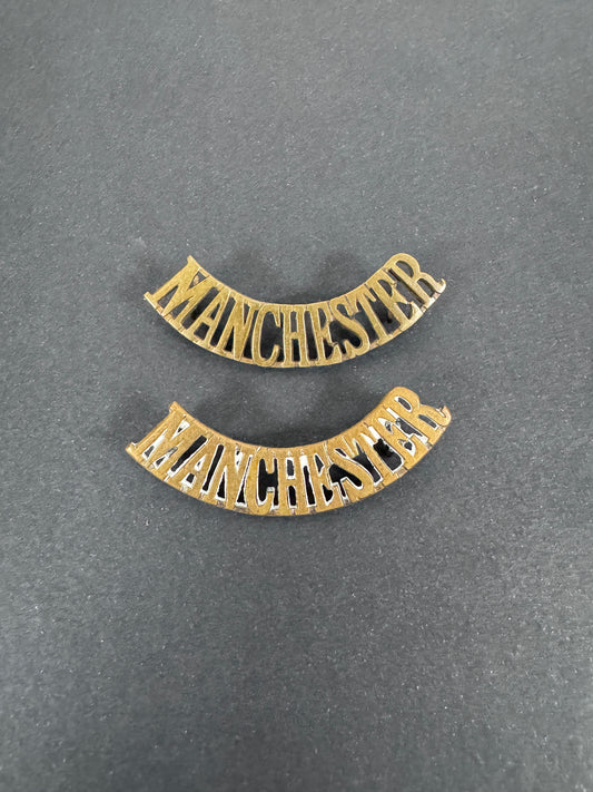 British Army Manchester Regiment Shoulder Title Badges (Pair) – A matching pair of original uniform shoulder titles of the...