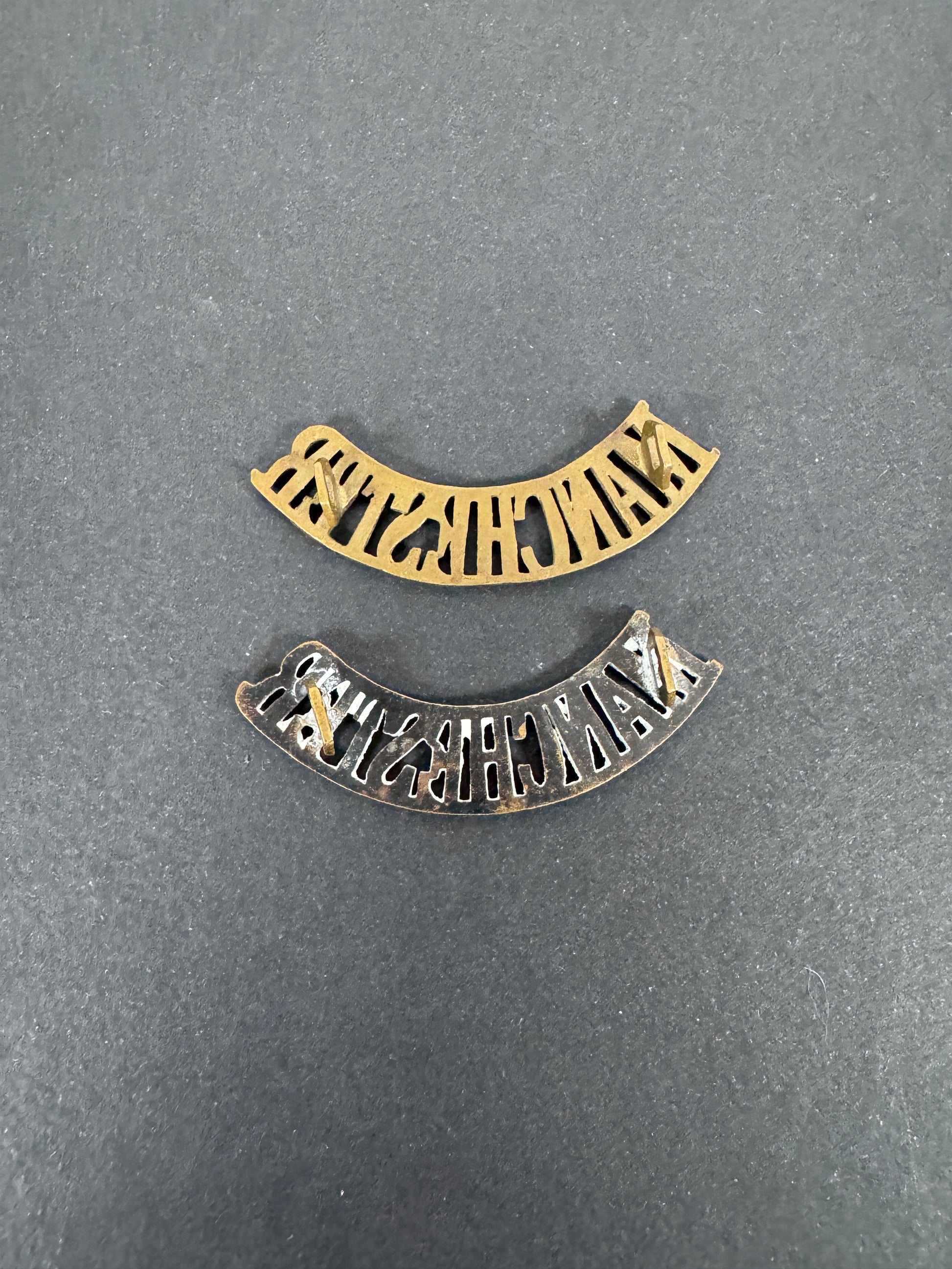 British Army Manchester Regiment Shoulder Title Badges (Pair) – A matching pair of original uniform shoulder titles of the...